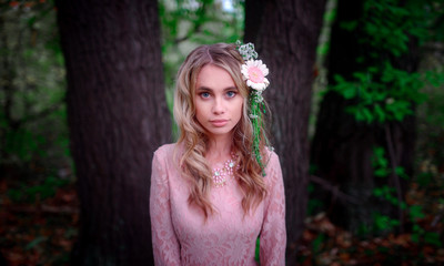beautiful woman with flowers in her blonde curls hair in laced pink dress posing  in fairytale forest