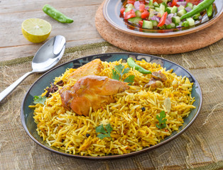 Chicken Biryani, a deleciously colorful rice dish filled with spicy marinated chicken  along with salad & raita.