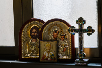 christian cross and icon of the Blessed Mother of God with baby Jesus and icon of Jesus Christ on the window in the house
