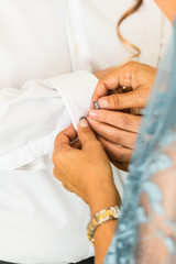 A groom putting on cuff-links as he gets dressed in his wedding day. Groom's suit
