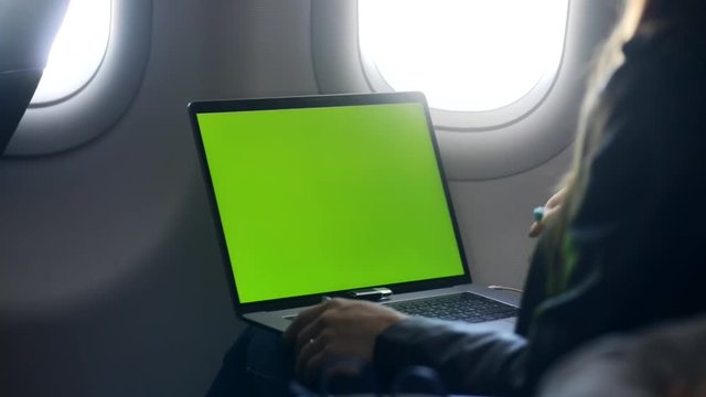 Concept of business journey. Young lady sitting with laptop in airplane cabin. She looking at monitor with empty screen or display with copy space and speaking