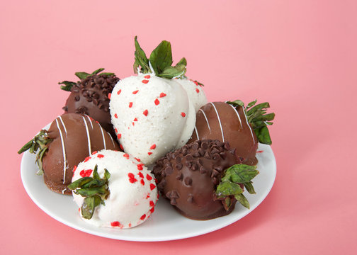 Variety of Chocolate covered strawberries on a plate. Dark, white and milk chocolate on a pink background. side view