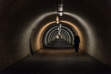 Female pedestrian walking in rush through underpass during summer night