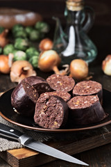 cut raw blood sausage, oil and vegetables on wood
