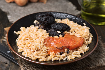 Homemade rice stew with black pudding and tomato in porcelain dish on wood
