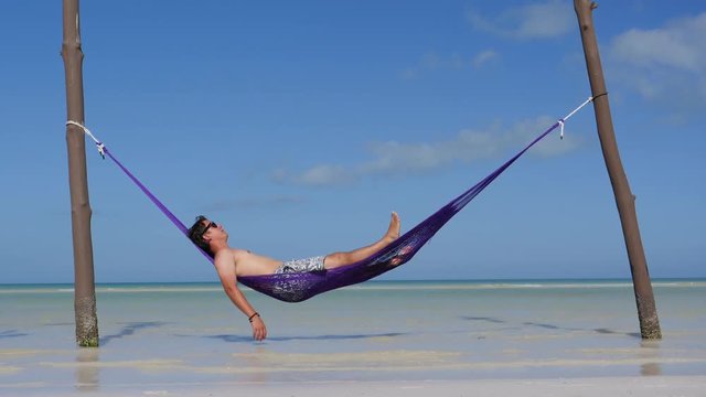 Happy young man on vacation laying and resting in hammock at sunset in hot summer on Mexico beach