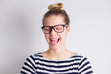 Crazy funny young blond woman in glasses showing tongue and smiling on white background