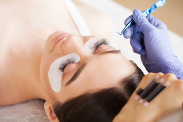 Fototapeta premium Eyelashes extensions. Fake Eyelashes. Eyelash Extension Procedure. Professional stylist lengthening female lashes. Master and a client in a beauty salon