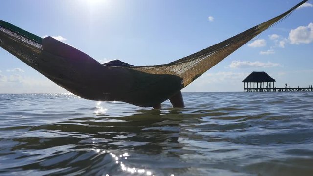 Happy young woman on vacation laying and resting in hammock at sunset in hot summer on Mexico beach