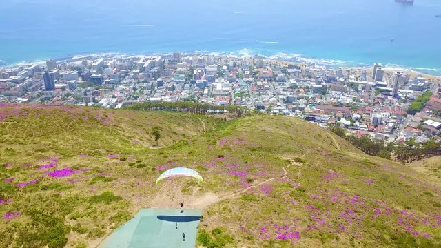 Drone aerial over paragliding and paragliders with the downtown city of Cape Town, South Africa, in background.