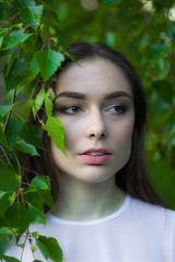 Portrait of a beautiful young woman on a background of green leaves, summer outdoors. Naturally beautiful woman smiling while standing among the green leaves.