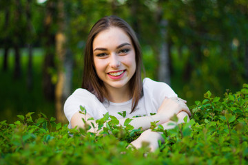 Portrait of a beautiful young woman on a background of green leaves, summer outdoors. Naturally beautiful woman smiling while standing among the green leaves.