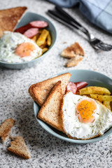 Breakfast with French fries, fried egg, sausage and toast on the table