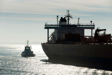 Obraz premium Southampton Water, Hampshire, England, UK. February 2019. Early morning against the light shot of a tug in attendance moving a broad beam oil tanker onto a berth at Fawley refinery.