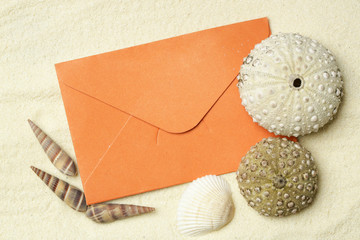 An orange blank envelope on white beach sand surrounded with seashells, travel concept template