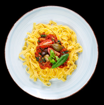 Tagliatelle with tomato sauce, olives, capern and basil leaves on rustic glazed clay plate - isolated on black background
