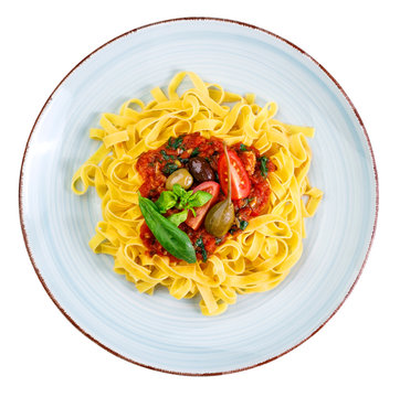 Tagliatelle with tomato sauce, olives, capern and basil leaves on rustic glazed clay plate - isolated on white background