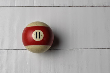 Old billiard ball number 11 striped white and red on white wooden table background, copy space