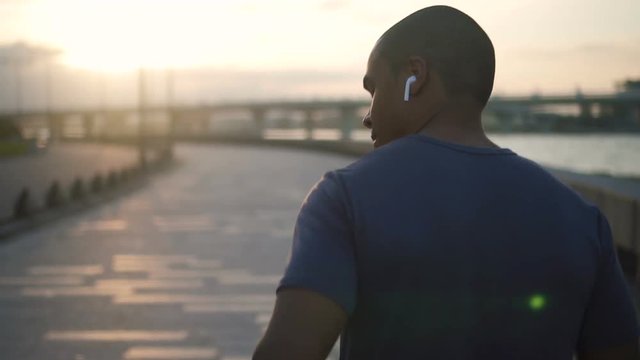 Attractive no face black healthy young man athlete exhausted and running with the sidewalk on bavkground listening to music using technology. close up fit african american model runner training in the