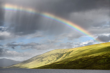 Rainbow and dark clouds over Loch a Chroisg ending at An Liathanach Hill near Badavanich Scottish Highlands Scotland UK