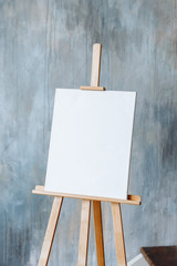 Wooden drawing easel with blank white sheet on wall background