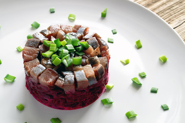 salted herring on beetroot, garlic, and mayo salad decorated with green onion