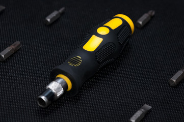 Black and yellow interchangable screwdriver with different bits surrounding. On dark dark background.