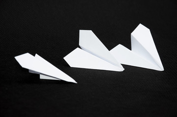 Three paper planes on dark background next to each other. Paper planes surrounding the scissors.