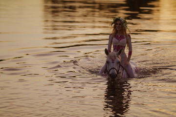 Blonde girl in white and red bodypain bathes with a horse in the lake at sunset.
