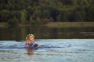 Blonde girl in white and red bodypain bathes with a horse in the lake at sunset.