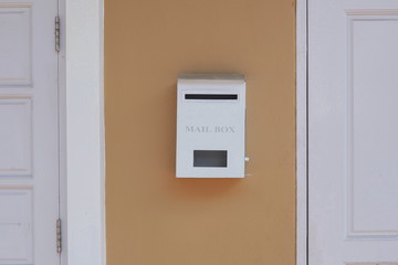 White mailbox between white wooden door and window on brown painted wall of house, home exterior decoration concept