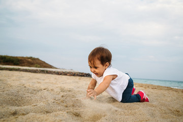 Small baby, little girl in white t-shirt creeping, playing in sand at the beach