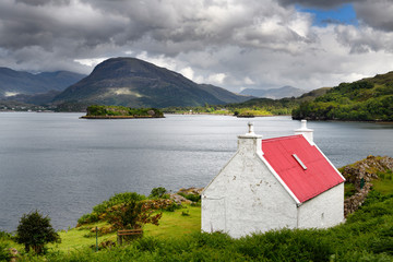 White stone house with red roof on Loch Shieldaig with Eilean an Inbhire Bhain Island and Ben Shieldaig Peak Scottish Highlands Scotland