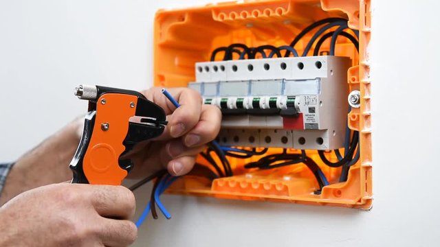 Video of the hands of the electrician technician who with the wire strippers prepares the electric cables in an electrical panel of a residential installation . Construction industry.