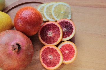 Oranges, lemons and pomegranates are lying on a wooden background.