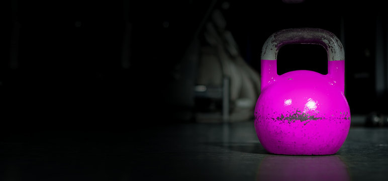 Heavy old used color kettlebell weight on the gym floor ready for fitness strength workout to build muscles with dark background and free copy space banner 