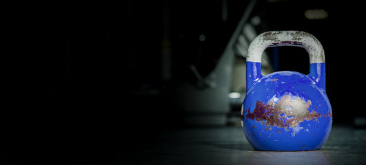 Heavy old used color kettlebell weight on the gym floor ready for fitness strength workout to build muscles with dark background and free copy space banner