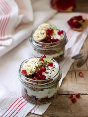 Granola with yogurt and fruit in glass jars on a wooden table. Rustic style.
