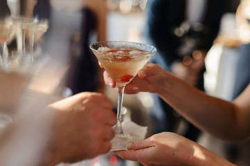 Close up shot of hand of young people clinking glasses with wine or champagne in front of bokeh background