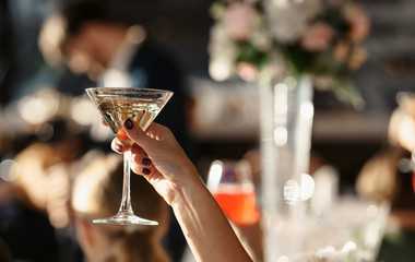 Close up shot of hand of young people clinking glasses with wine or champagne in front of bokeh background