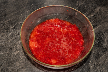 Making of strawberries with sugar on black table in white tile kitchen