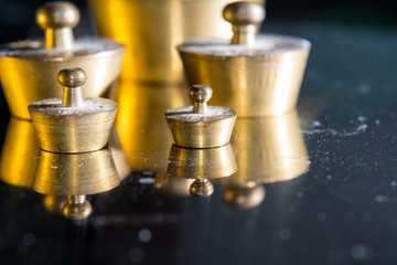 brazen old weights for scales with different weight, standing on a metal shining surface with reflection, dust on the weights, blur background