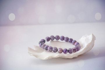 An amethyst bracelet in a seashell with a white and purple bokeh background.