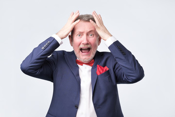 Oh no concept. Surprised, shocked man in blue suit holding hands up near head