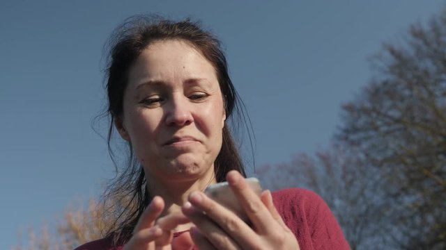 Beautiful woman texting the boyfriend while siting outside in a park. Woman chatting with an online dating happy and smiley. 4K video