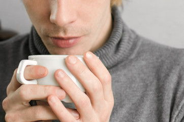 young man in a gray sweater with a Cup of coffee in his hands