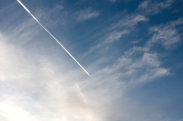 Jet airplane leaves white trail in the  blue and cloudy  sky.