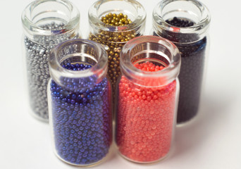 Multicolored beads in glass jars. Beads are poured on a white background. Plastic multi-colored polymers. Plastic pillets.