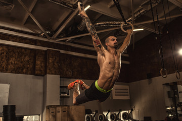 Male athlete working out on gymnastics rings at the crossfit gym - obrazy, fototapety, plakaty