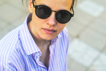 Portrait of a Young Smiling Women in Sunglasses. Young Happy Woman in a Striped Shirt Walks Down the Street at Sunset Time